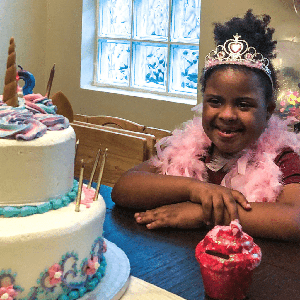 Girl wearing tiara looking at unicorn cake