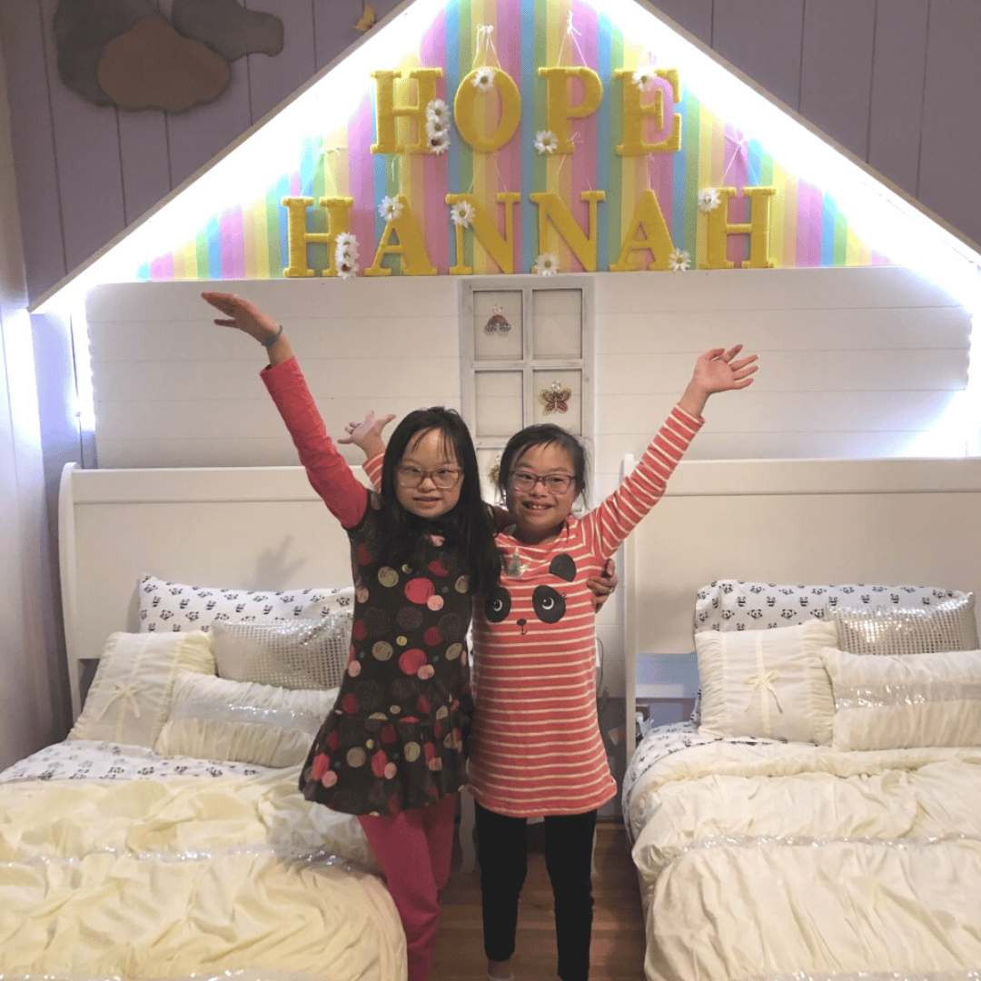 Hannah and her twin sister Hope who both have Down syndrome smiling in their newly decorated bedroom