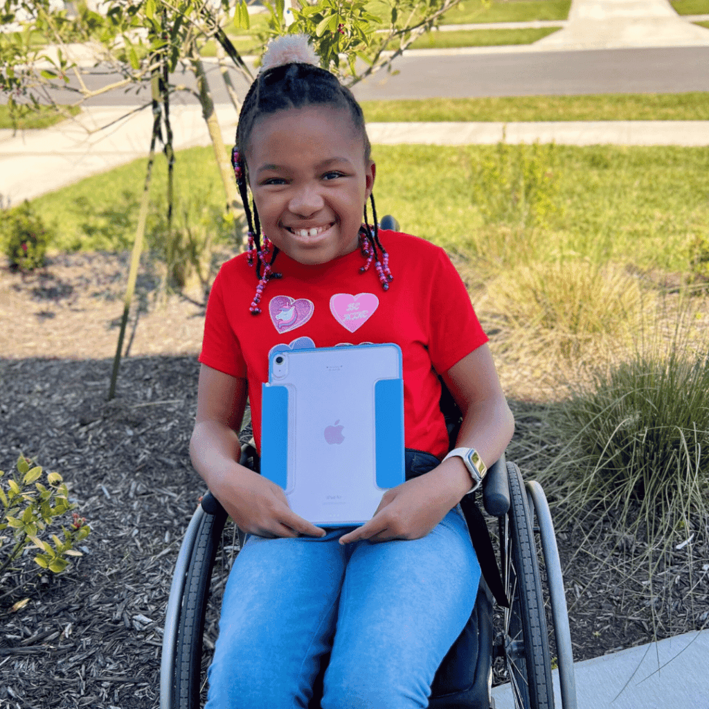 11-year-old girl sitting in her wheelchair smiling as she holds her new iPad
