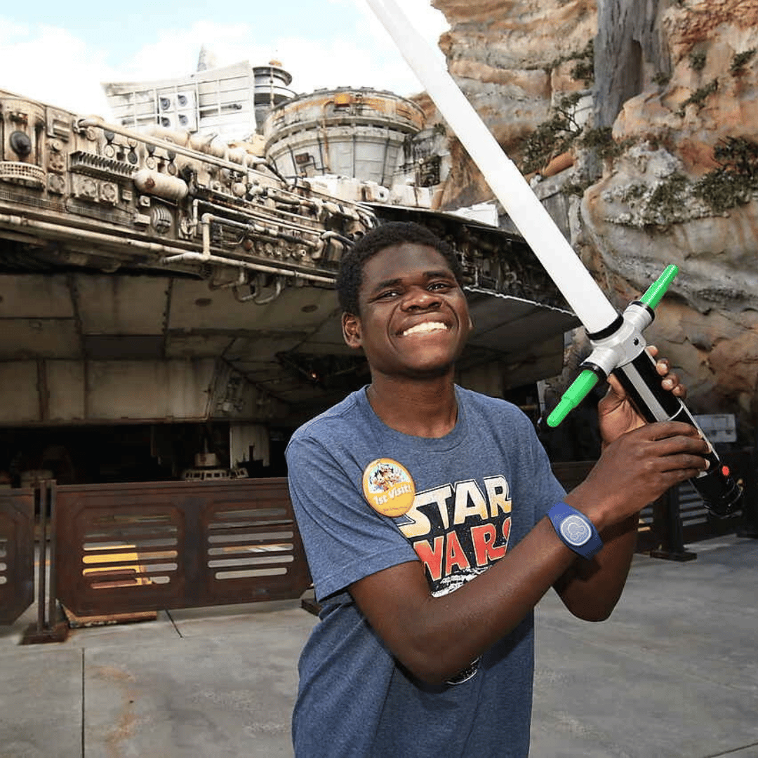Teen boy with developmental delay smiling as he poses with his lightsaber a Disney's Hollywood Studio.