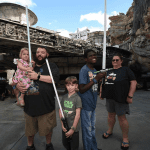 Teen boy with developmental delay, smiling as he poses with his family and their lightsabers at Disney's Hollywood Studio.